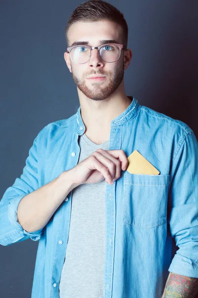 Joven sosteniendo una tarjeta de crédito de pie sobre fondo gris. Joven empresario. —  Fotos de Stock