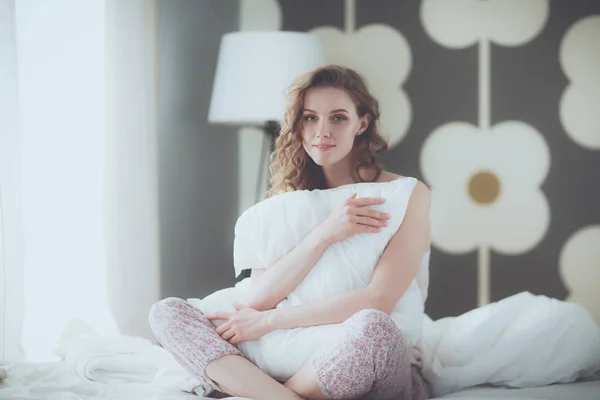 Νέα γυναίκα που κρατά ένα μαξιλάρι, ενώ κάθεται στο κρεβάτι της. — Φωτογραφία Αρχείου