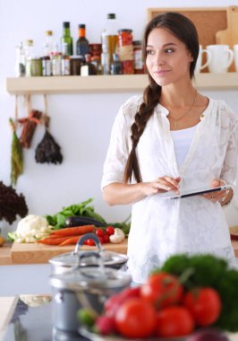 Mutfakta yemek yapmak için tablet bilgisayar kullanan genç bir kadın.