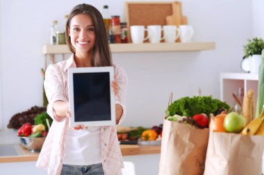 Mutfakta yemek yapmak için tablet bilgisayar kullanan genç bir kadın.