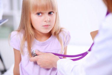 Kadın doktor ameliyatta steteskopla çocuğu muayene ediyor.