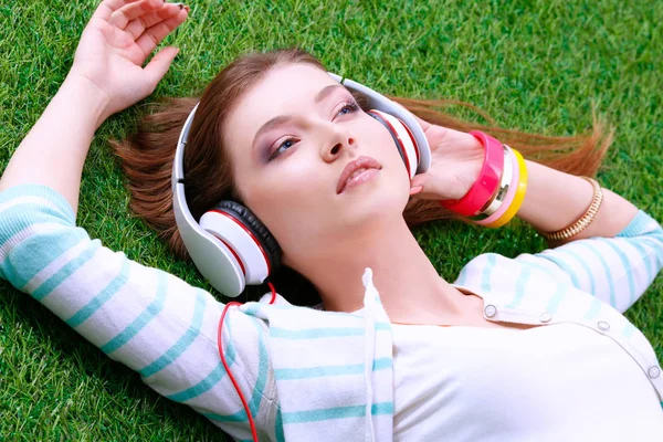 푸른 잔디에 누워 음악을 듣고 젊은 여자 — 스톡 사진