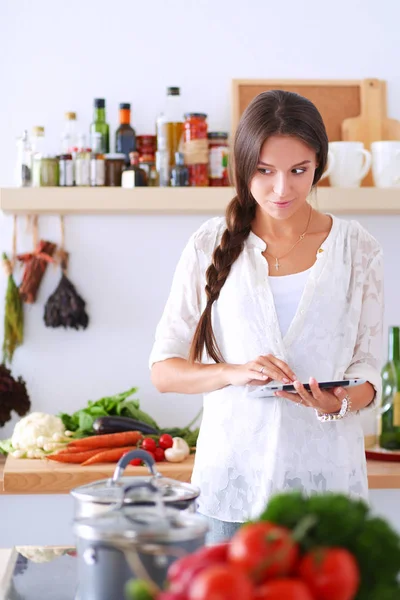 Mutfakta yemek yapmak için tablet bilgisayar kullanan genç bir kadın.