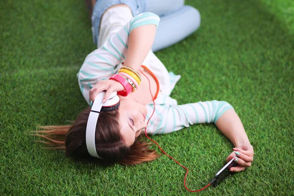 Jonge vrouw luisteren naar de muziek, liggend op groen gras — Stockfoto