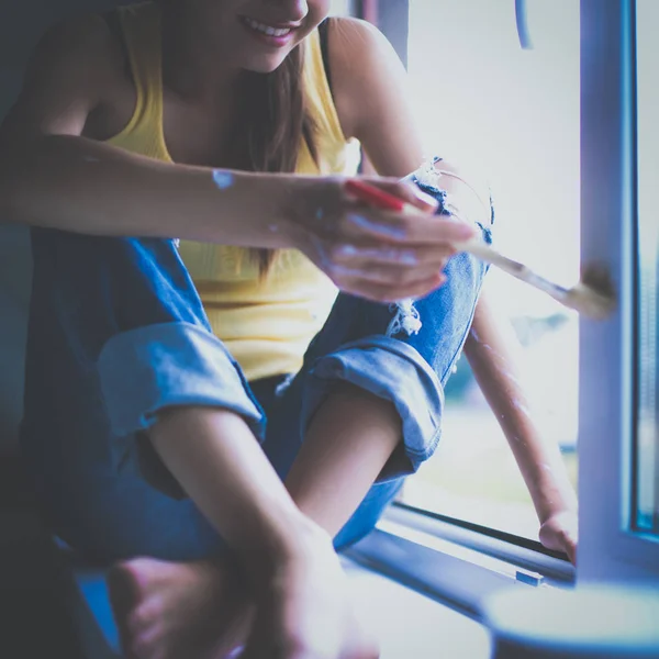 Mujer pintando la pared de un apartamento con un pincel cuidadosamente terminando alrededor del marco de la ventana —  Fotos de Stock