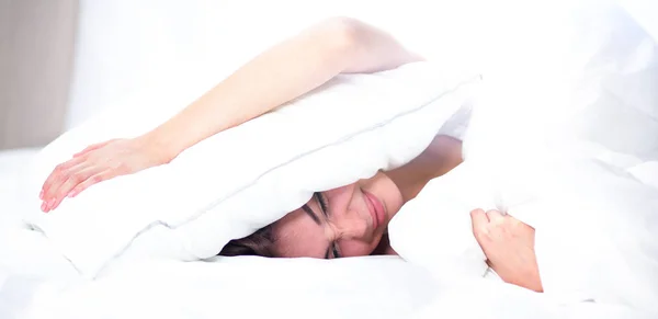 Kadın yatakta uzanıyor ve kulaklarını yastıkla kapatıyor. — Stok fotoğraf
