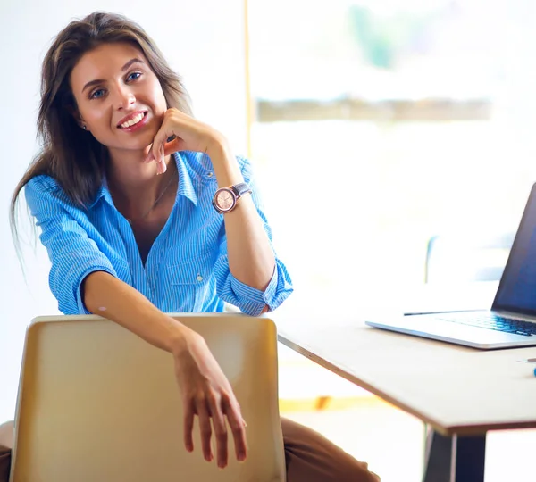 Ofis masasında dizüstü bilgisayarıyla oturan genç bir kadın.