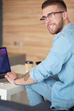 Genç bir telefonu kullanarak ve bir dizüstü bilgisayarda çalışan adam. Öğrenci manifatura telefon.