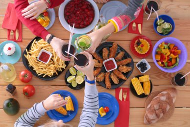 Ahşap masada otururken birlikte yemek yiyen bir grup insanın üst düzey görüntüsü. Masada yemek var. İnsanlar fast food yiyor..