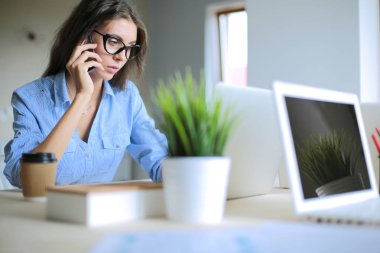 Ofis masasında oturan ve cep telefonuyla konuşan genç ve güzel bir iş kadını. İş kadını