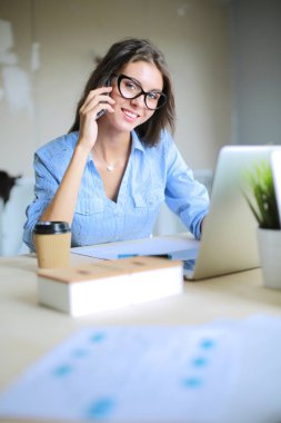Ofis masasında oturan ve cep telefonuyla konuşan genç ve güzel bir iş kadını. İş kadını