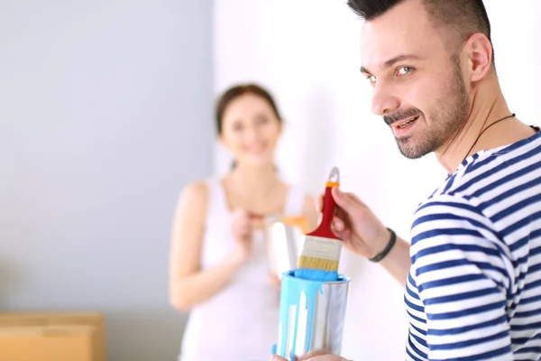 Portret van een vrolijk glimlachend jong stel dat de binnenmuur van een nieuw huis schildert. jong stel — Stockfoto