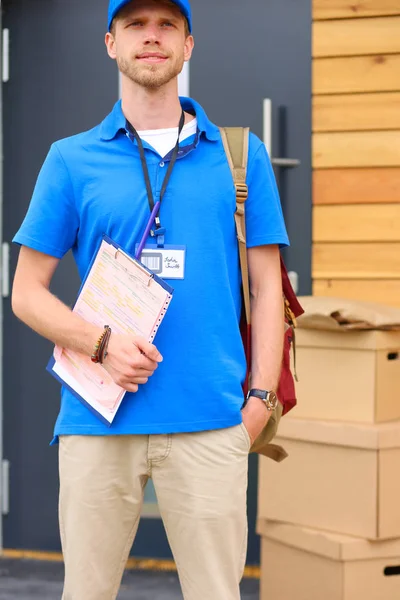 Repartidor sonriente con uniforme azul que entrega la caja de paquetes al destinatario: concepto de servicio de mensajería. Repartidor sonriente en uniforme azul —  Fotos de Stock