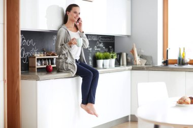 modern mutfakta otururken cep telefonu kullanan kadın.