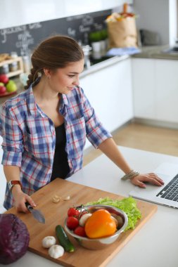 Masanın yanındaki mutfakta sebze doğrayan genç bir kadın..
