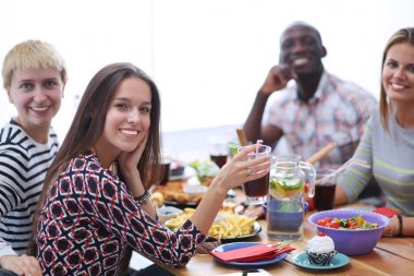 Ahşap masada otururken birlikte yemek yiyen bir grup insanın üst düzey görüntüsü. Masada yemek var. İnsanlar fast food yiyor..