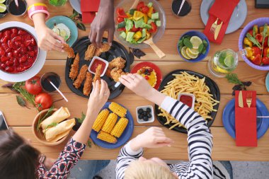 Ahşap masada otururken birlikte yemek yiyen bir grup insanın üst düzey görüntüsü. Masada yemek var. İnsanlar fast food yiyor..