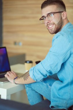 Genç bir telefonu kullanarak ve bir dizüstü bilgisayarda çalışan adam. Öğrenci manifatura telefon.