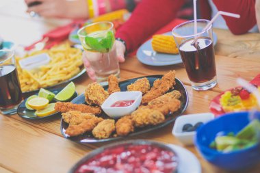 Ahşap masada otururken birlikte yemek yiyen bir grup insanın üst düzey görüntüsü. Masada yemek var. İnsanlar fast food yiyor..