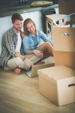 Genç bir çift yeni ev içinde hareket. Oturma ve açma sonra rahatlatıcı. Bir şey üstünde laptop arıyorum. Genç Çift