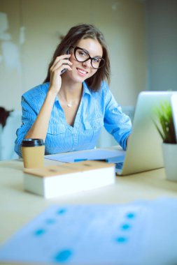 Ofis masasında oturan ve cep telefonuyla konuşan genç ve güzel bir iş kadını. İş kadını