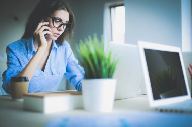 Ofis masasında oturan ve cep telefonuyla konuşan genç ve güzel bir iş kadını. İş kadını