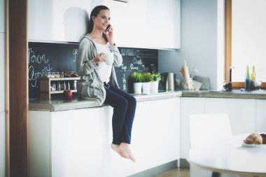 modern mutfakta otururken cep telefonu kullanan kadın.