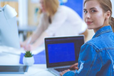 İki genç kadın masada enstrümanlar, planlar ve dizüstü bilgisayarlarla oturuyor..