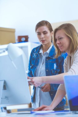 Masanın yanında duran iki genç kadın enstrüman, plan ve dizüstü bilgisayarla.