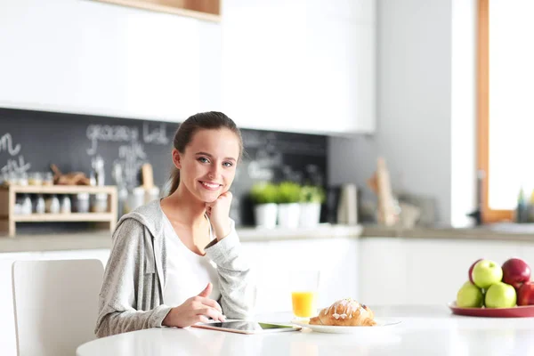 Ung kvinna med apelsinjuice och tablett i köket. — Stockfoto