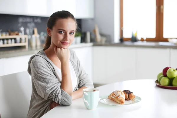 Kvinna som dricker te med söt croissant på köksbordet. — Stockfoto