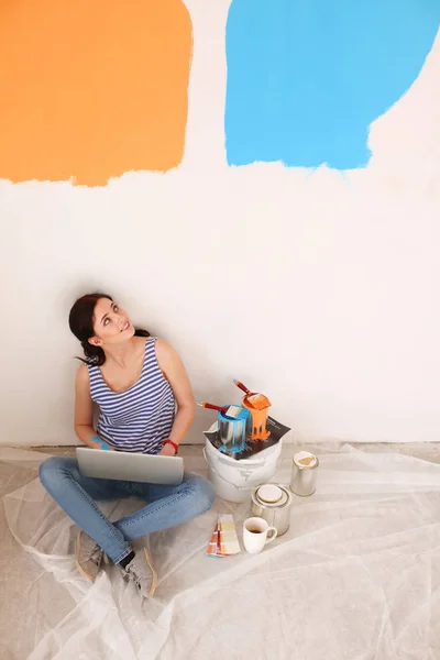 Retrato de mujer joven mientras pinta nuevo apartamento, sentado con el ordenador portátil. Mujer joven con portátil — Foto de Stock