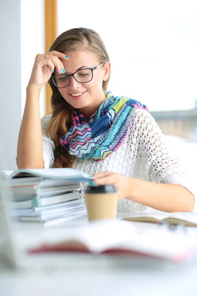 Ung kvinna som sitter vid ett skrivbord bland böcker. Studerande — Stockfoto