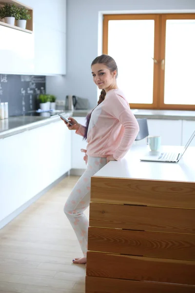 Kvinnan använder mobiltelefon stående i modernt kök. — Stockfoto