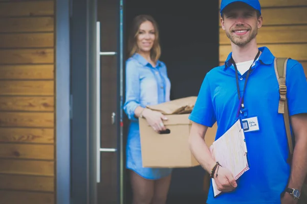 Usmívající se doručovatel v modré uniformě doručující balíček příjemci - koncept kurýrní služby. Usmívající se doručovatel v modré uniformě — Stock fotografie