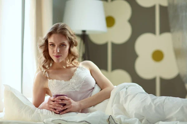 Νεαρή γυναίκα πίνοντας καφέ ή τσάι ξαπλωμένοι στο κρεβάτι. — Φωτογραφία Αρχείου