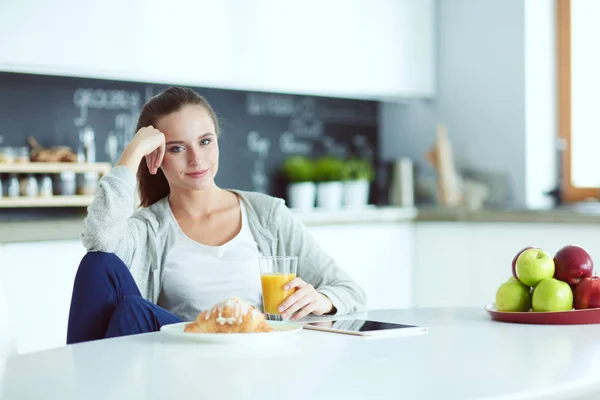 Ung kvinna med apelsinjuice och tablett i köket. — Stockfoto