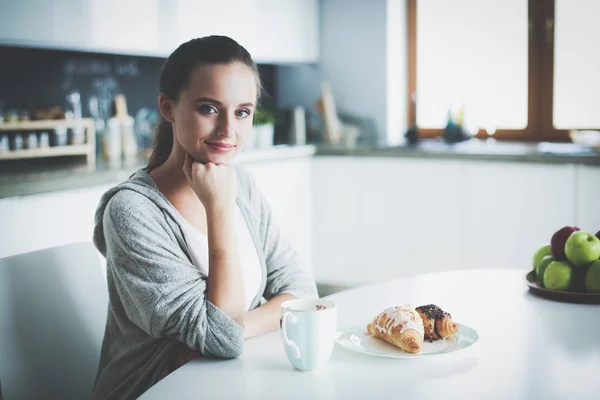 Kvinna som dricker te med söt croissant på köksbordet. — Stockfoto