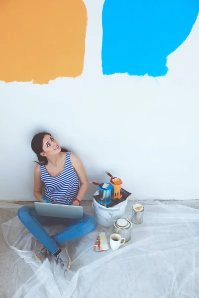 Retrato de mujer joven mientras pinta nuevo apartamento, sentado con el ordenador portátil. Mujer joven con portátil — Foto de Stock