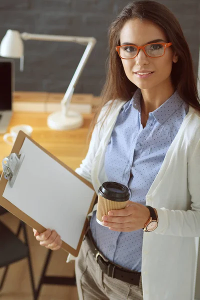 Młoda kobieta stojąca przy biurku z folderem na laptopie i filiżanką kawy. Miejsce pracy. Bizneswoman. — Zdjęcie stockowe