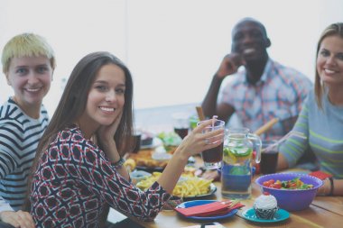 Ahşap masada otururken birlikte yemek yiyen bir grup insanın üst düzey görüntüsü. Masada yemek var. İnsanlar fast food yiyor..