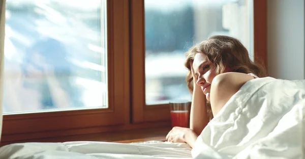 Kvinna ligger i sängen på morgonen nära fönster — Stockfoto