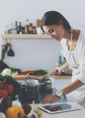 Mutfakta yemek yapmak için tablet bilgisayar kullanan genç bir kadın.