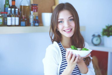 Genç bir kadın salata yiyor ve karışık bir şey tutuyor.
