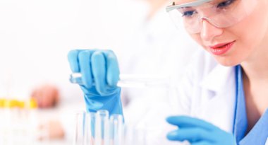 Kadın araştırmacı, beyaz arka planda izole edilmiş ilaç şişeleri ve mataralarla çevrili.