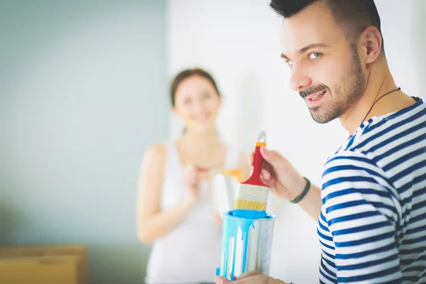 Retrato de feliz joven pareja sonriente pintando la pared interior de la casa nueva. pareja joven —  Fotos de Stock