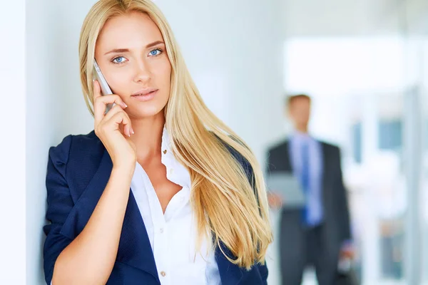 Geschäftsfrau steht gegen Bürofenster und telefoniert — Stockfoto