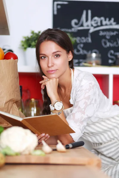 Ung kvinna läser kokbok i köket, letar efter recept — Stockfoto