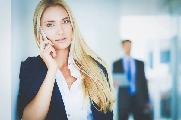 Zakenvrouw staat tegen kantoorraam te praten op mobiele telefoon — Stockfoto