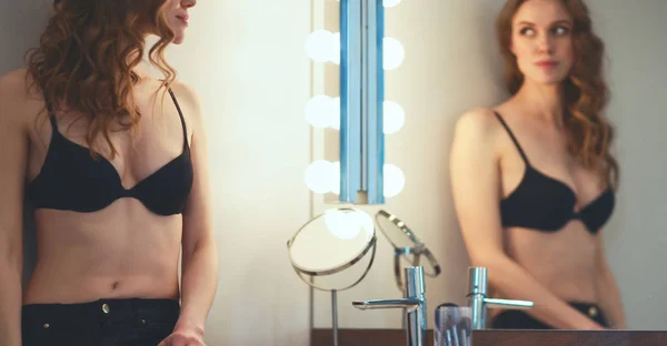 Молодая женщина смотрит на себя в зеркало в ванной комнате — стоковое фото